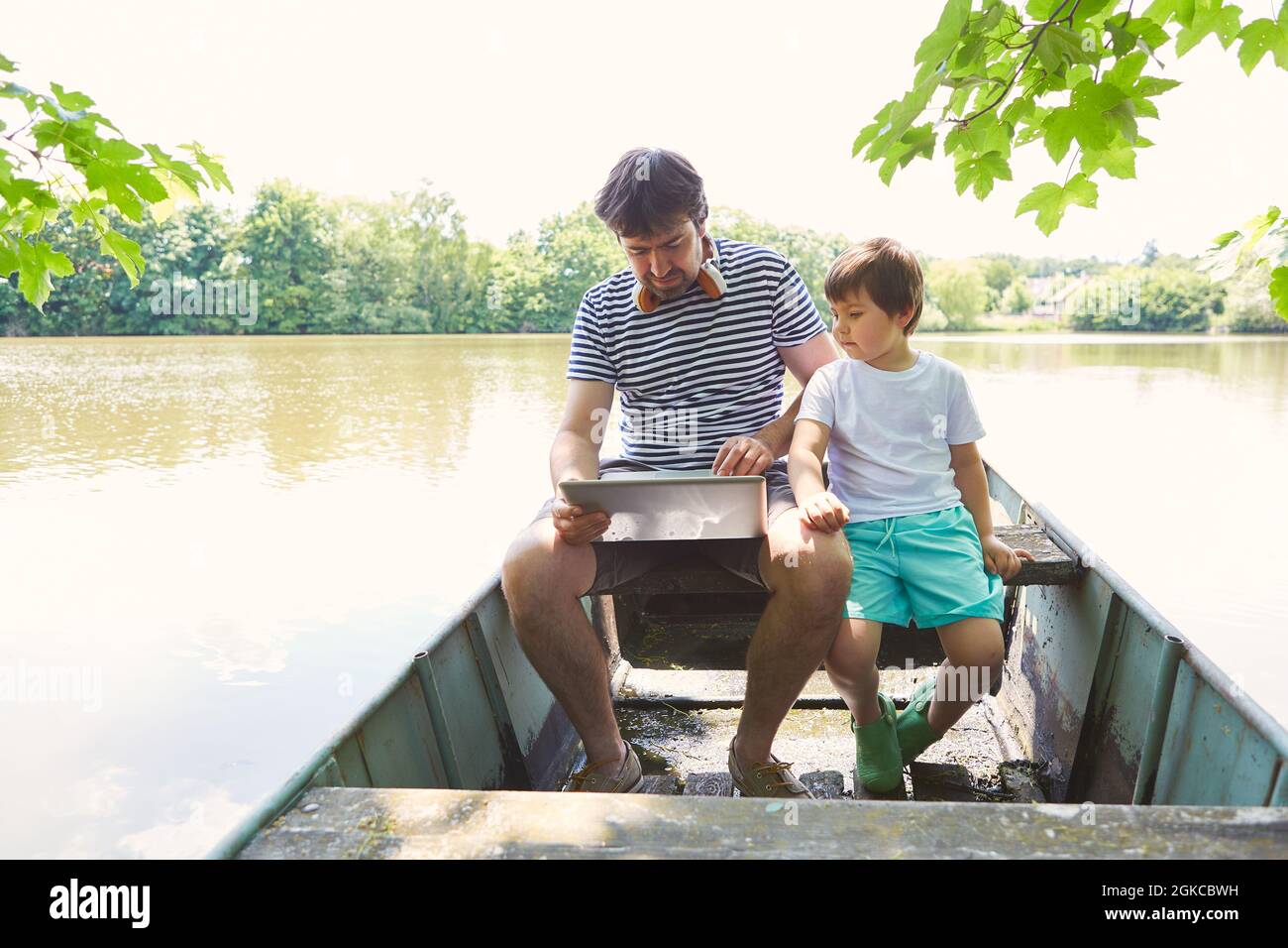 Singolo padre e figlio con PC portatile in una barca sul lago come freelance Foto Stock