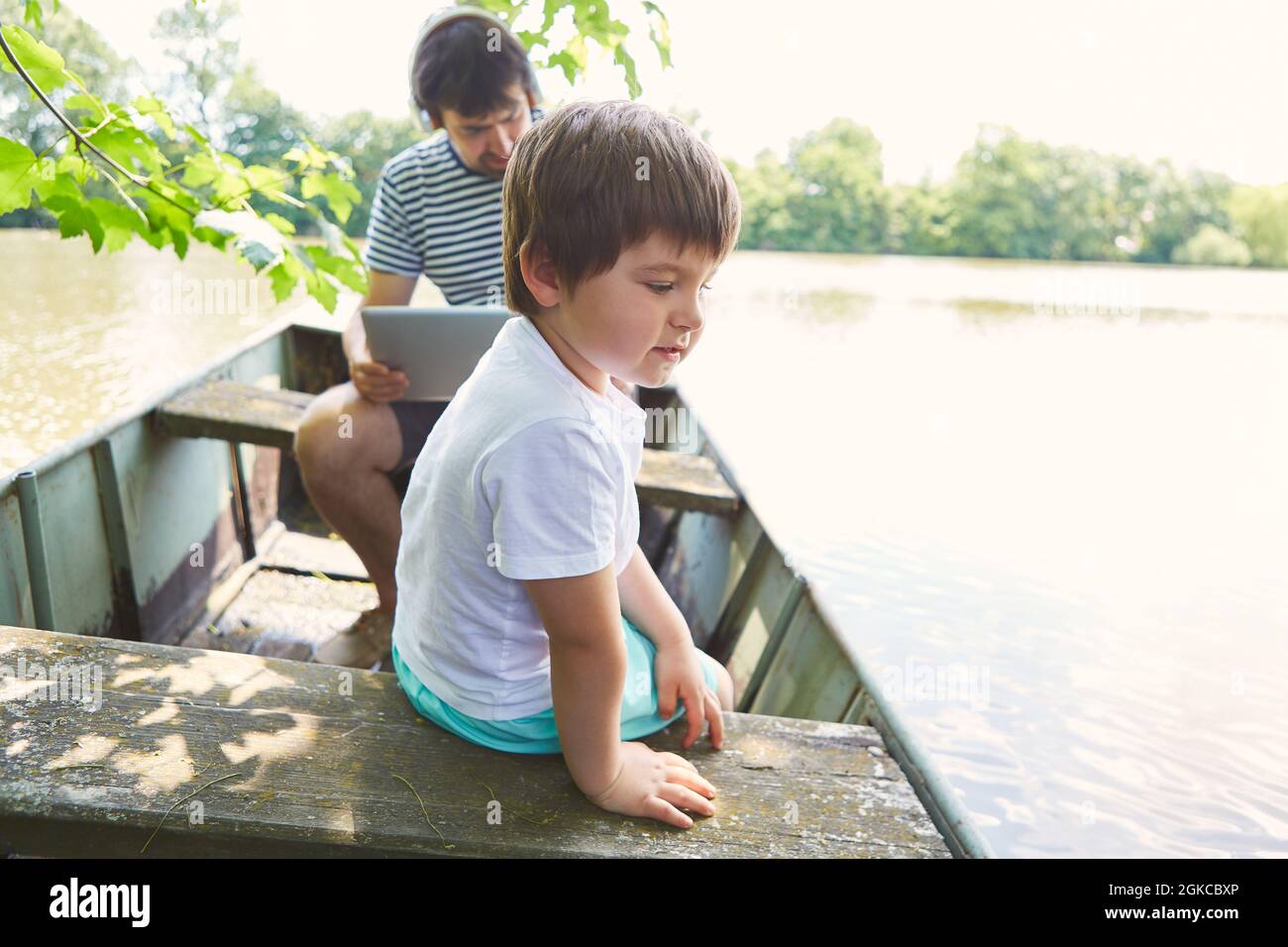 Ragazzo in barca su un lago durante le vacanze estive con padre sul portatile in background Foto Stock