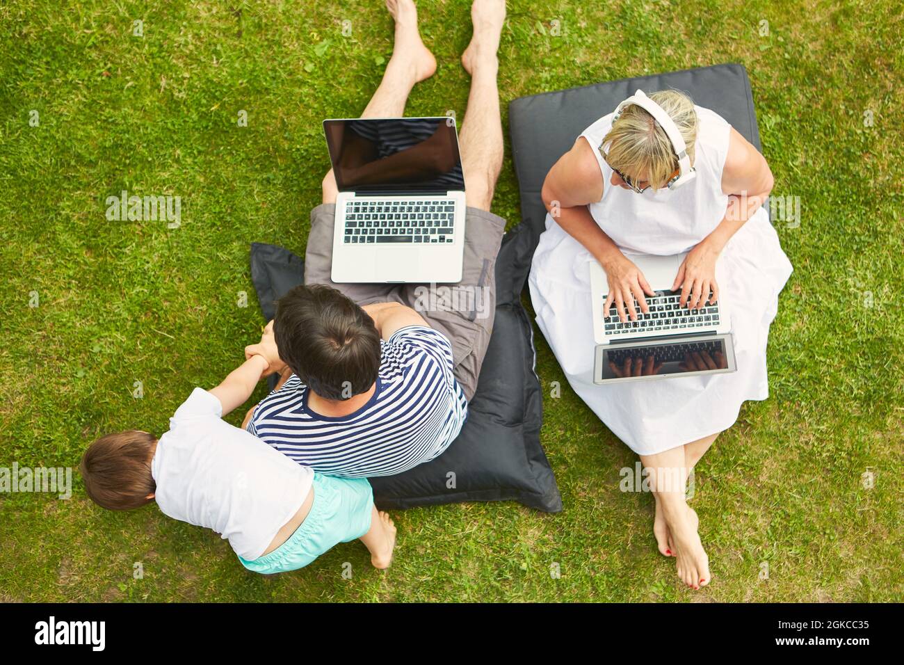 I genitori lavorano sul computer in giardino come un ufficio domestico con un bambino come distrazione Foto Stock