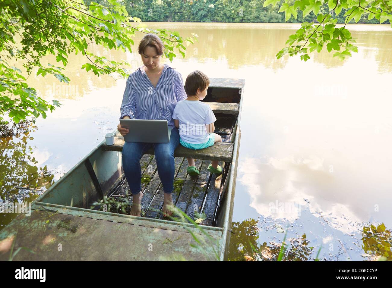 Madre e figlio che usano il computer portatile in una barca sul lago durante le vacanze estive Foto Stock