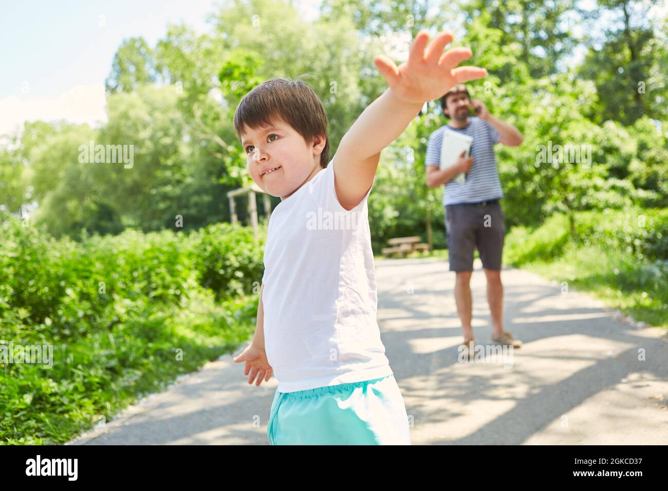 Bambini che giocano nel parco durante le vacanze estive con il padre che fanno una telefonata mobile in background Foto Stock