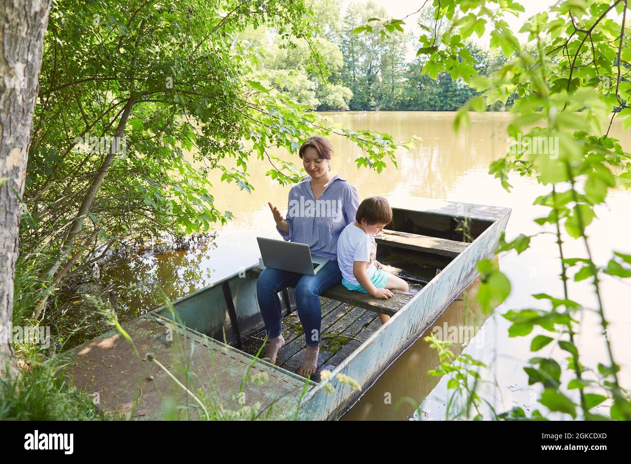 Donna come madre e freelance con PC portatile in una barca al lago con suo figlio Foto Stock