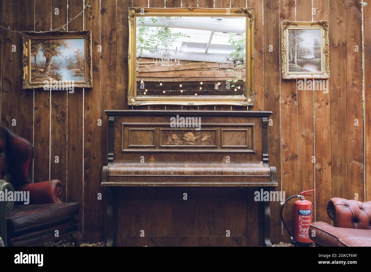 Un antico pianoforte rustico con uno specchio sopra e una parete in legno intemperiato Foto Stock