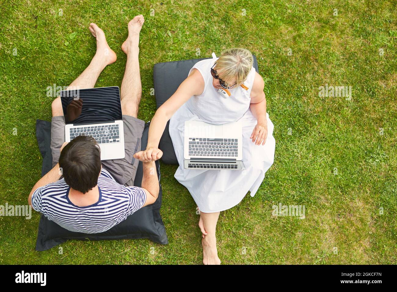 Coppia seduta mano in mano sul prato in giardino al computer come un freelance dall'alto Foto Stock
