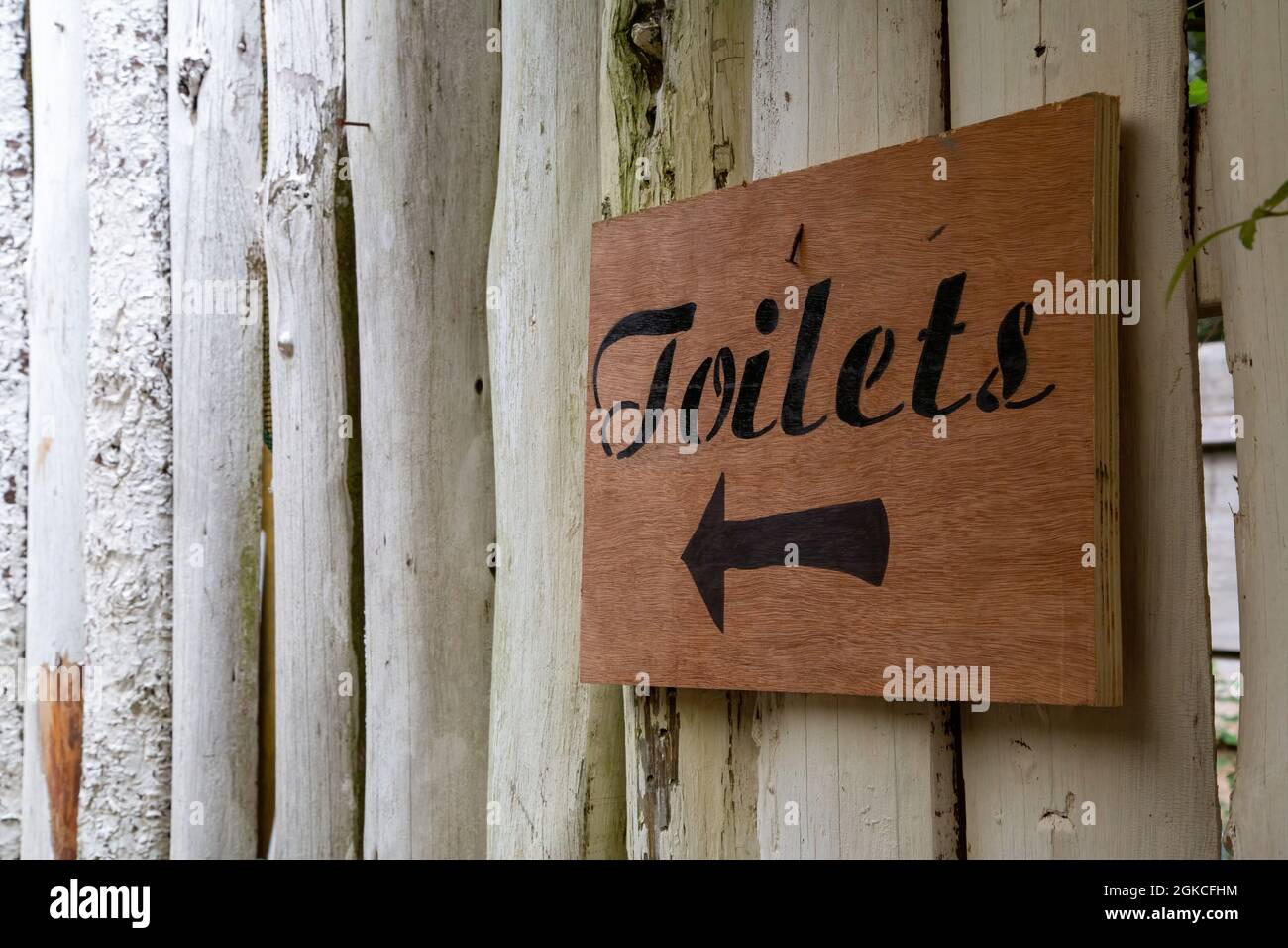 un cartello rustico in legno su un muro che punta ai servizi igienici Foto Stock