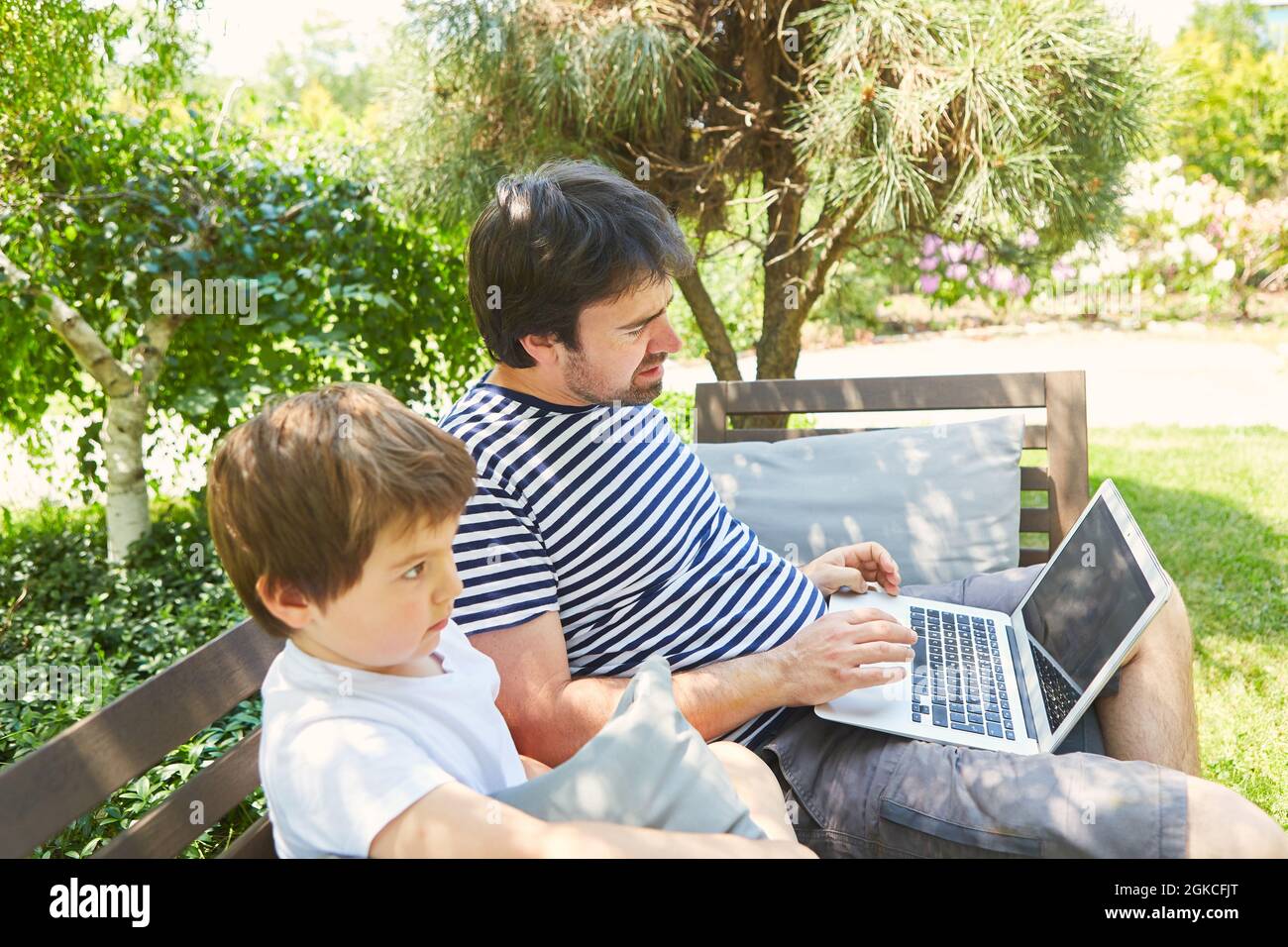 Padre e figlio usano il computer portatile in giardino d'estate mentre lavorano Foto Stock