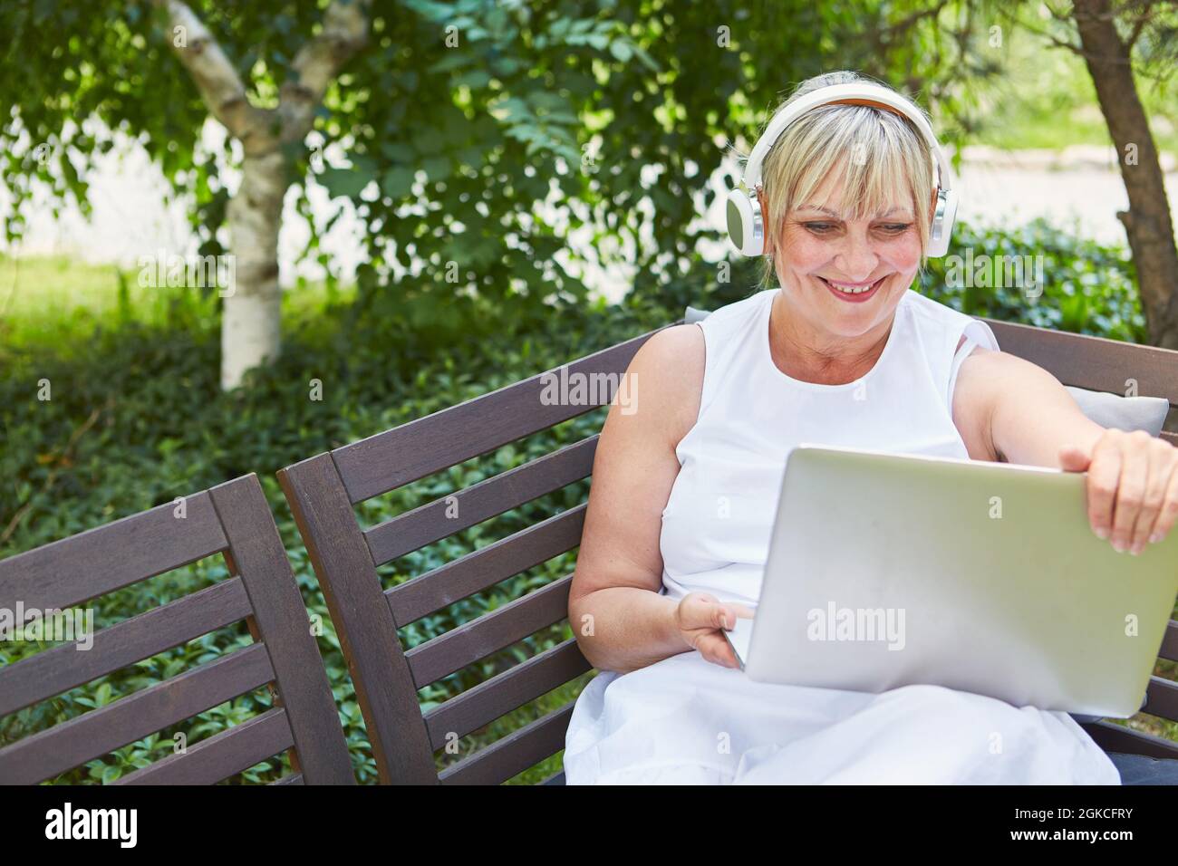 Donna di affari sorridente sul computer portatile mentre video chiacchiera in giardino in estate Foto Stock
