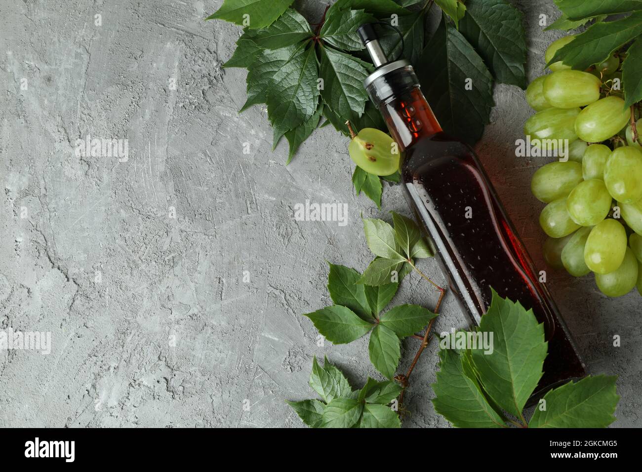 Bottiglia di aceto, uva e foglie su tavola grigia Foto Stock