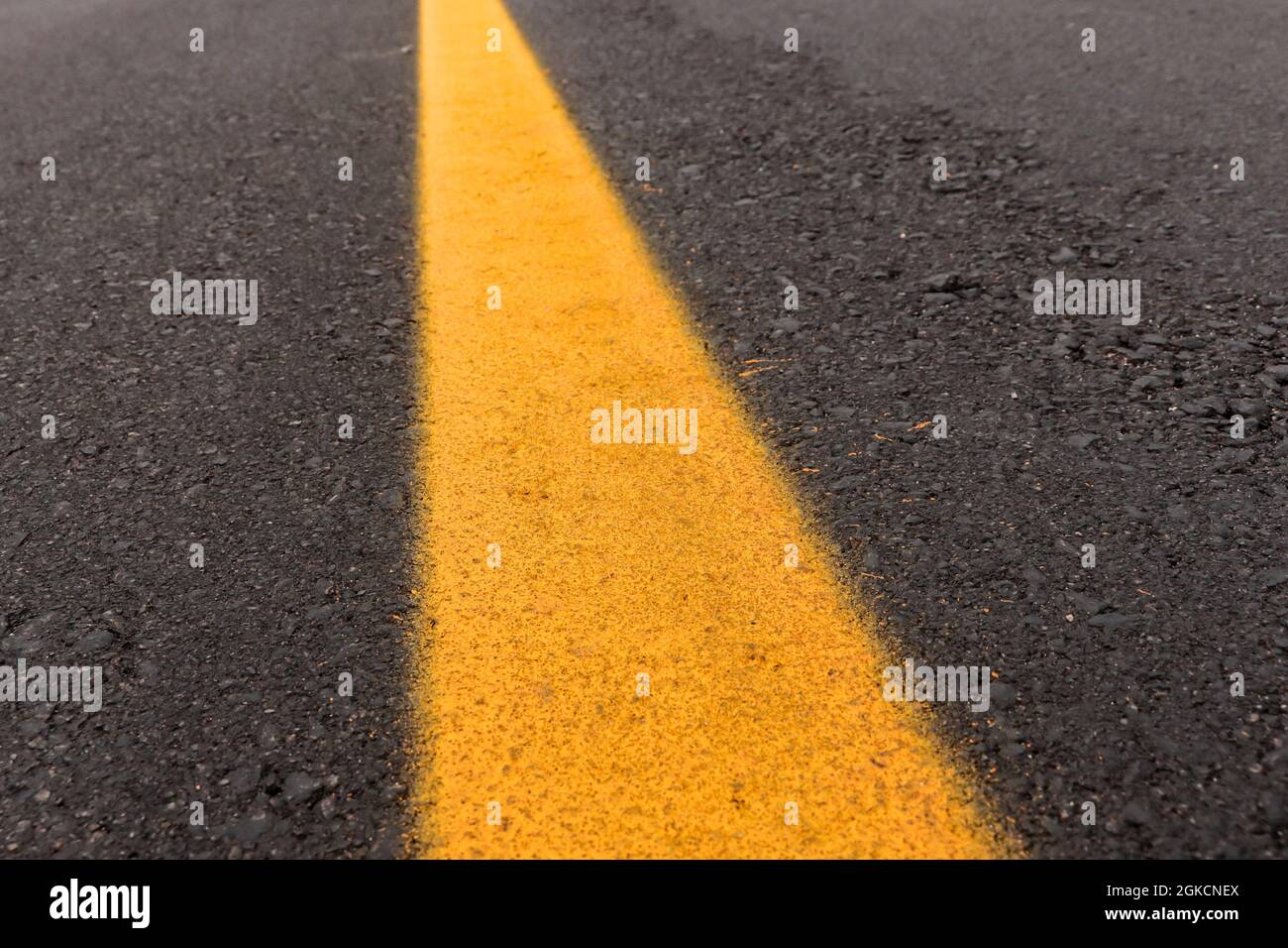 Asfalto tracciato appena fatto con un po' di sporco e la sua consistenza, con una striscia gialla dipinta al centro dell'immagine Foto Stock