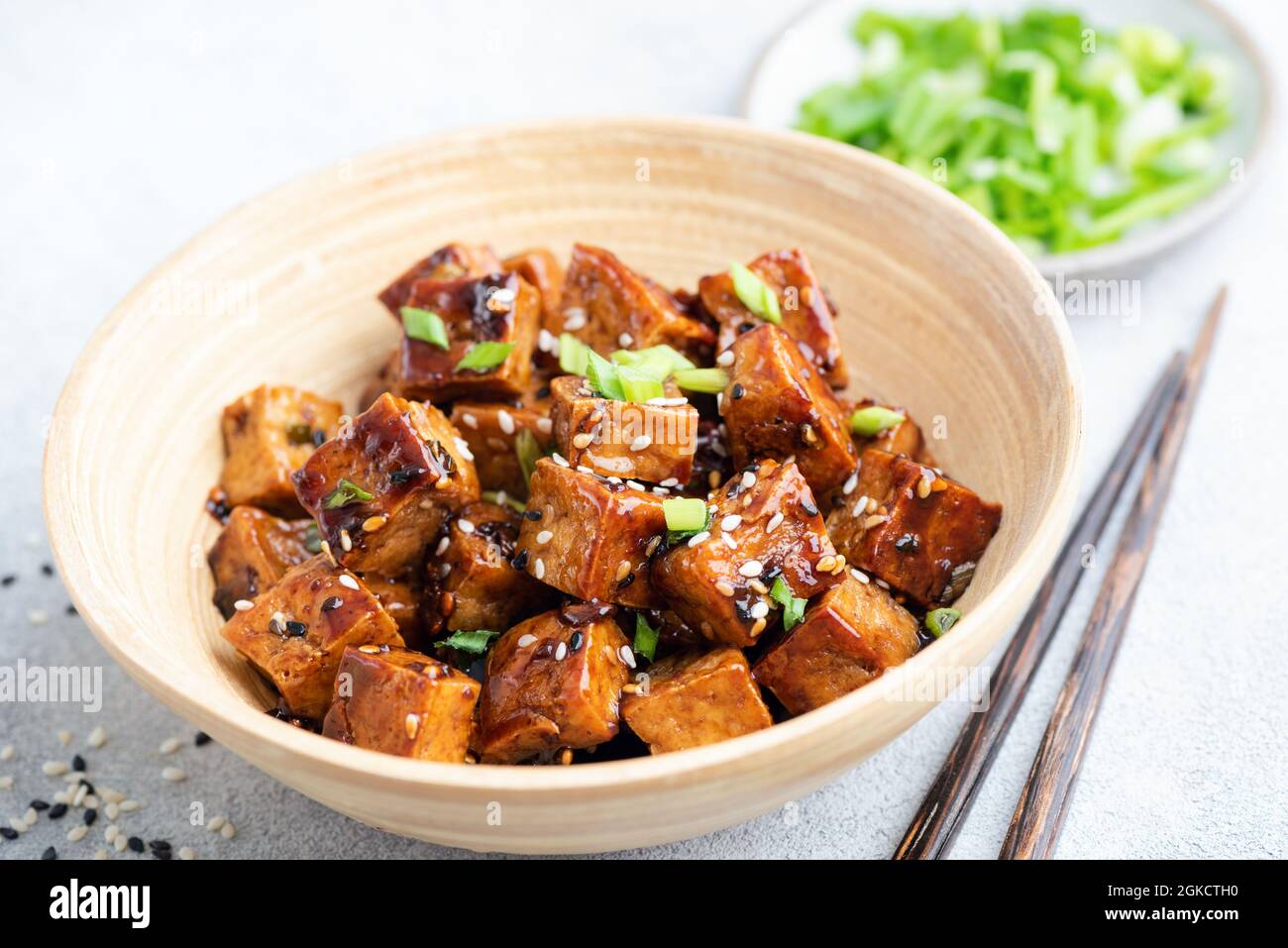 Cubetti di tofu fritti con salsa e semi di sesamo in una ciotola di bambù, vista dal primo piano Foto Stock
