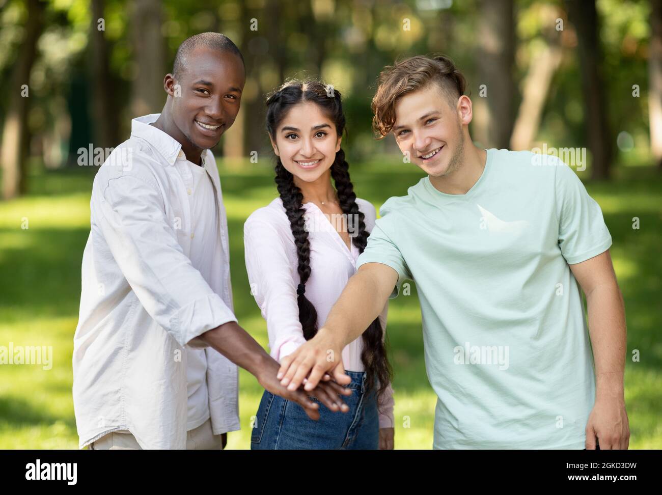 Istruzione e concetto di unità. Gli studenti internazionali felici si accatastano le mani, camminando nel campus universitario Foto Stock