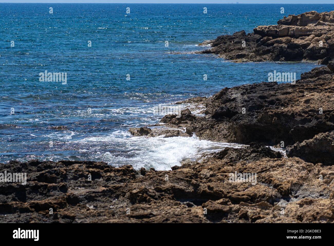 Surf in mare, onde blu del mare Mediterraneo a Cipro. Spiaggia di pietra rocciosa. Giorno d'estate. Paradiso di sole. Giornate di sole. Vista sulla spiaggia di Foto Stock