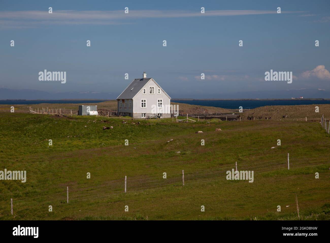 Una tipica casa costruita in legno sull'isola di Flatey in Islanda con pecore che pascolo sul terreno di pascolo grezzo in una zona di bassa popolazione Foto Stock