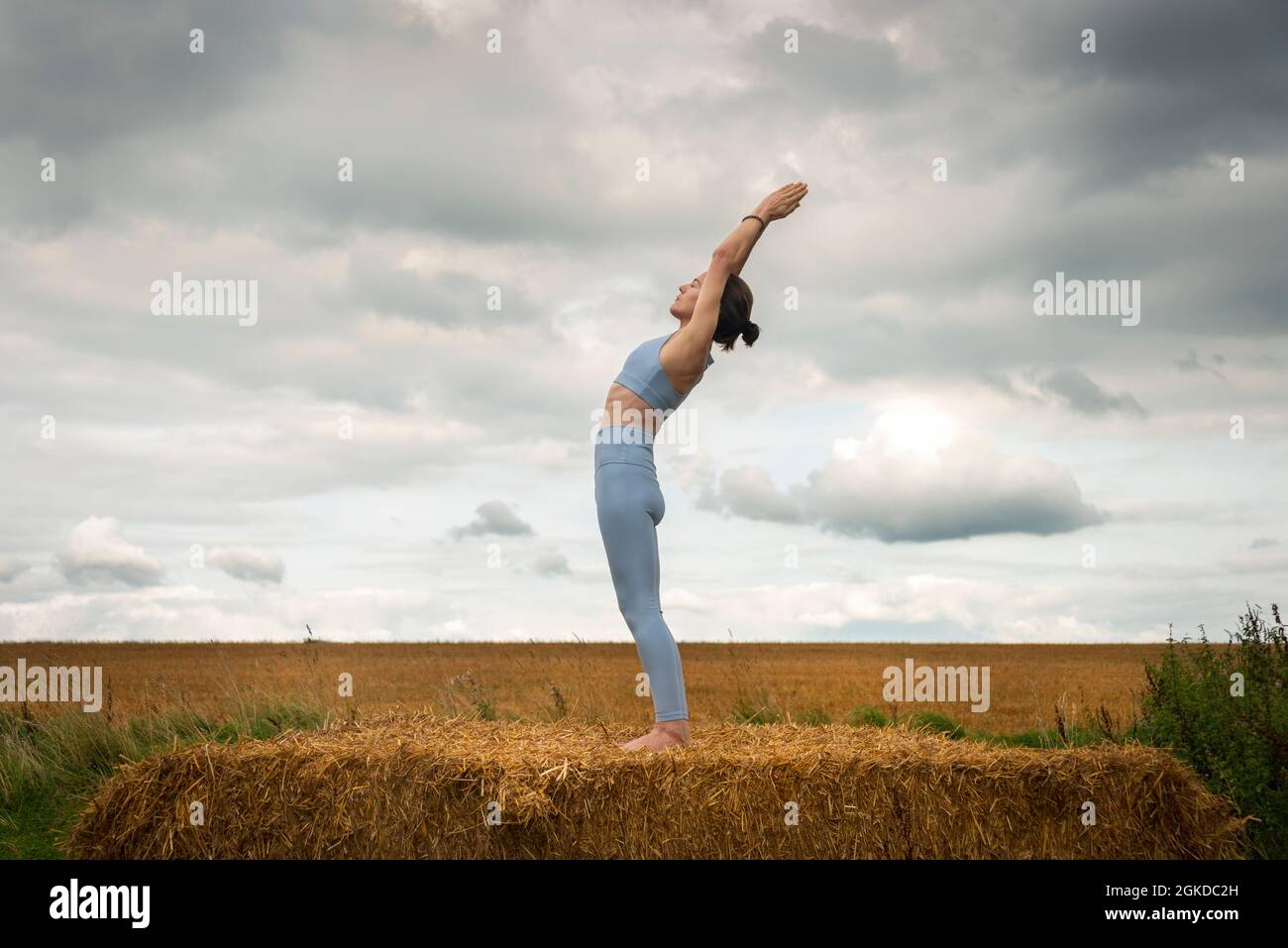 Donna caucasica che fa backbend in piedi su una balla di paglia in un campo, concetto di yoga di idoneità. Foto Stock