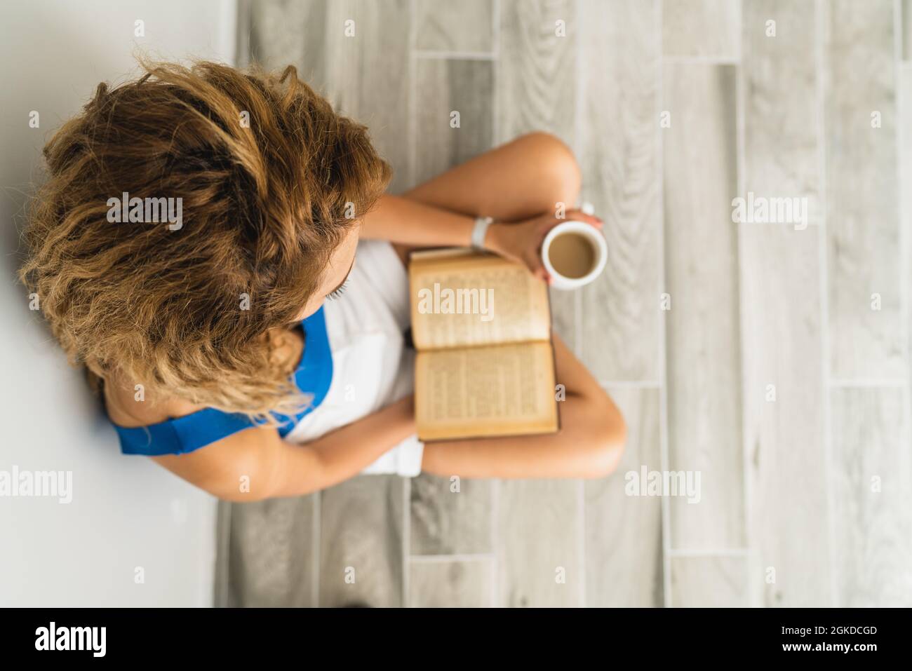 La giovane donna intellettuale si siede a terra e beve una tazza di caffè, mentre sta leggendo un libro. Foto di alta qualità Foto Stock