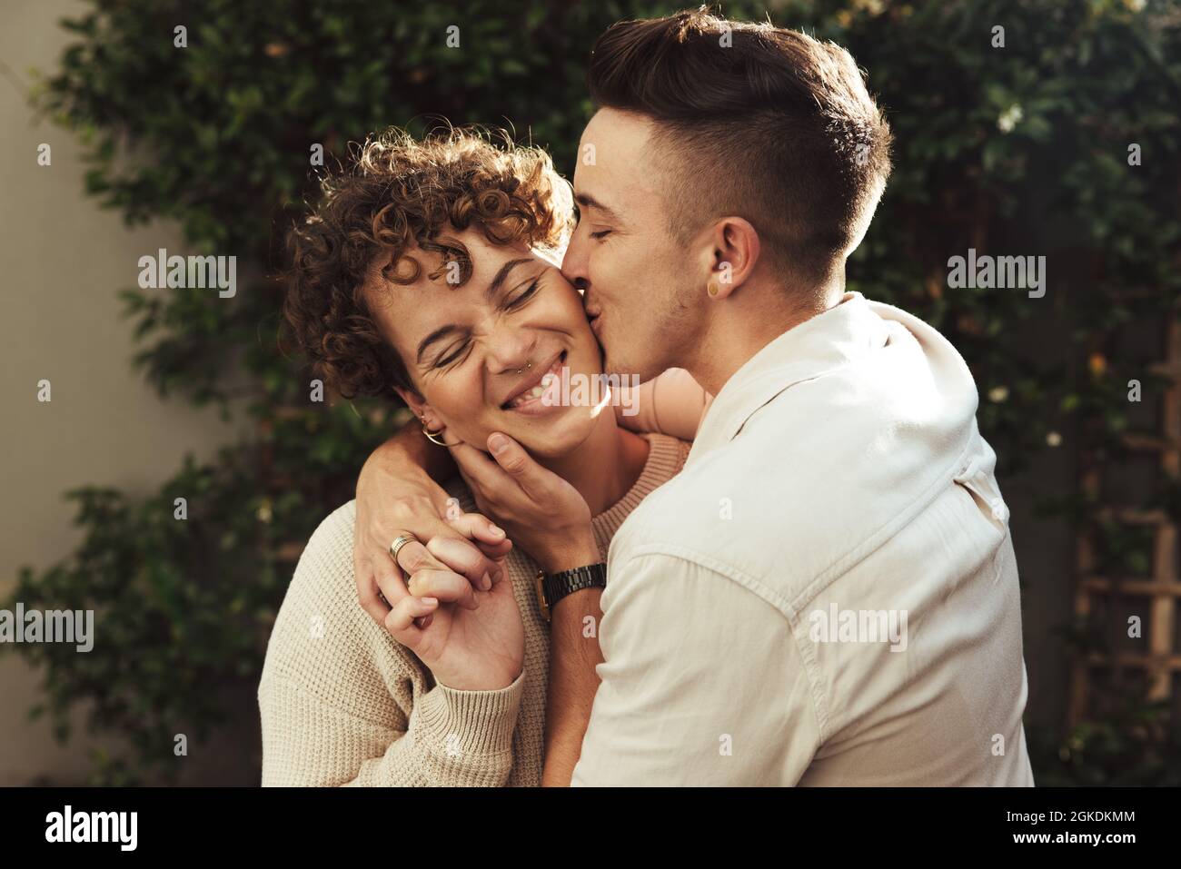 Il giovane affettuoso bacia la sua ragazza all'aperto. Il giovane romantico bacia la sua ragazza sulla guancia mentre la abbraccia. Giovane coupl LGBTQ+ Foto Stock