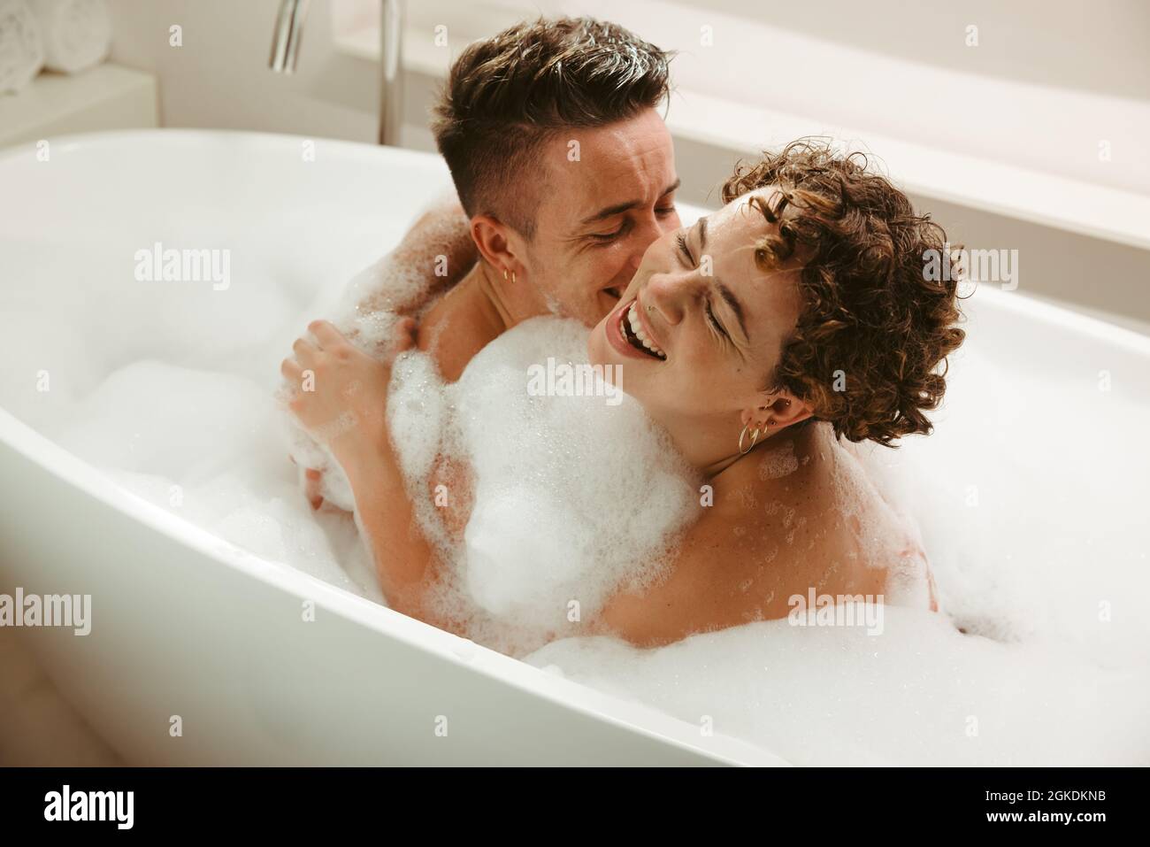 Felice giovane coppia queer divertirsi nella vasca da bagno. Romantica coppia giovane che si gode un bagno bolla insieme a casa. Giovane coppia LGBTQ+ che spende qualit Foto Stock