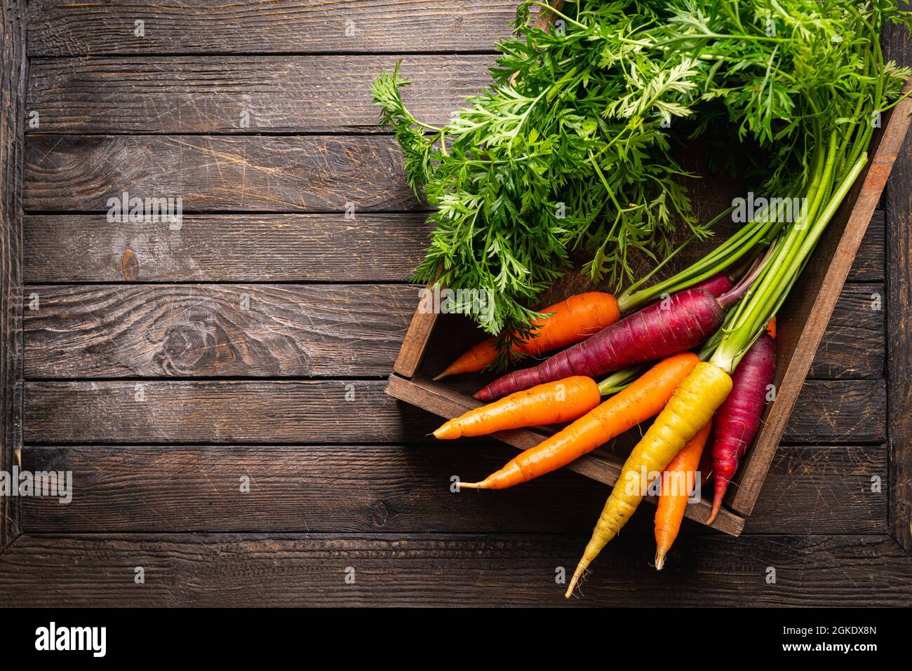 Colorata carota arcobaleno con le loro foglie verdi in una scatola su sfondo di legno, vista dall'alto Foto Stock
