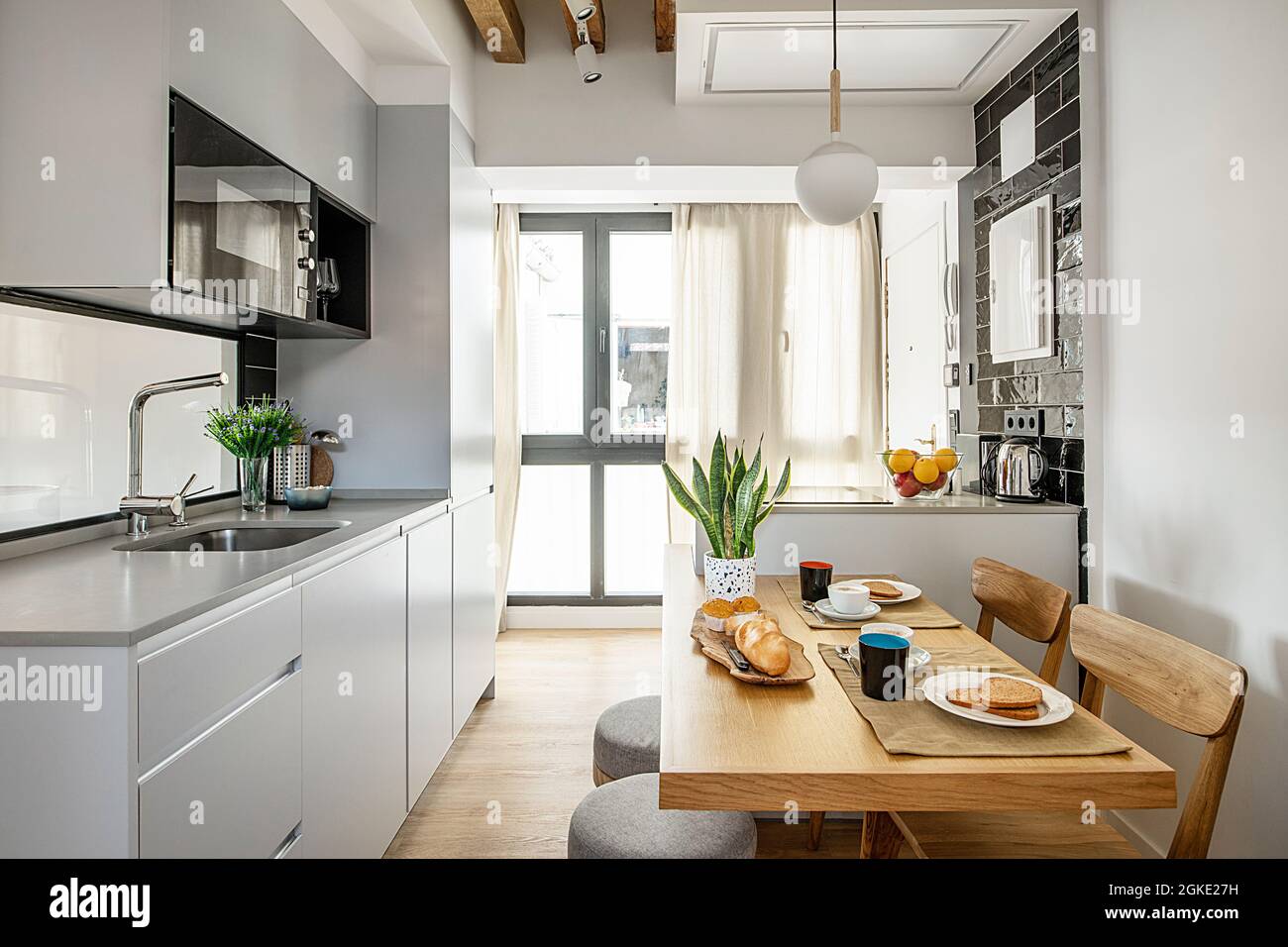 Cocina en pequeño apartamento de alquiler vacacional con el desayuno servido en la mesa del Office con cafe, bollos y tostadas. Foto Stock