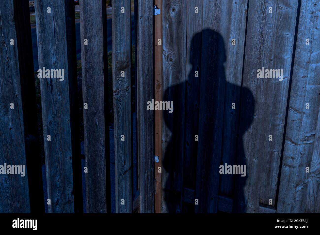 Ombra umana in piedi su recinzione di legno durante il crepuscolo Foto Stock