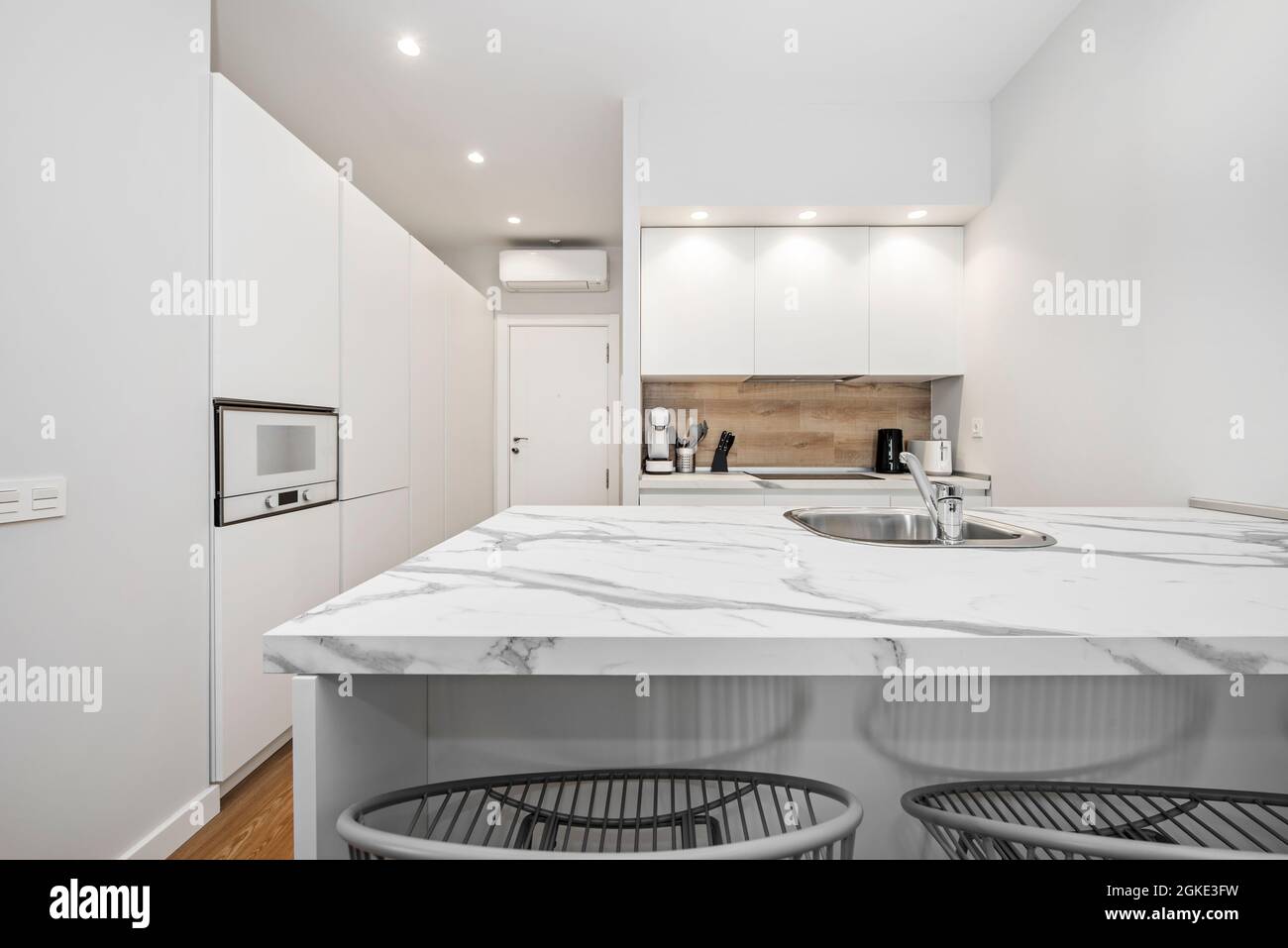 Isola cucina bianca con top in marmo bianco venato con lavandino e cucina e  armadi di stoccaggio sullo sfondo in una moderna unità di affitto per le  vacanze Foto stock - Alamy