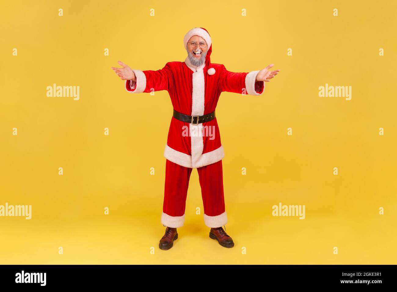 Uomo anziano felice a tutta lunghezza con barba grigia che indossa il costume di babbo natale alzando le mani per abbracciare, accogliente e sorridente felice di riunione. IO Foto Stock