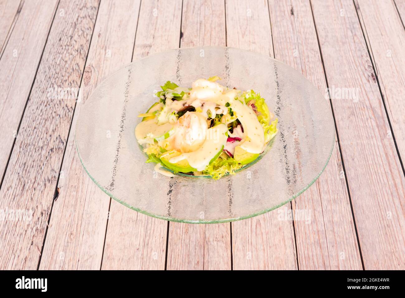Insalata di gamberi e avocado con lattuga con salsa di panna su vetro trasparente su tavola di legno Foto Stock
