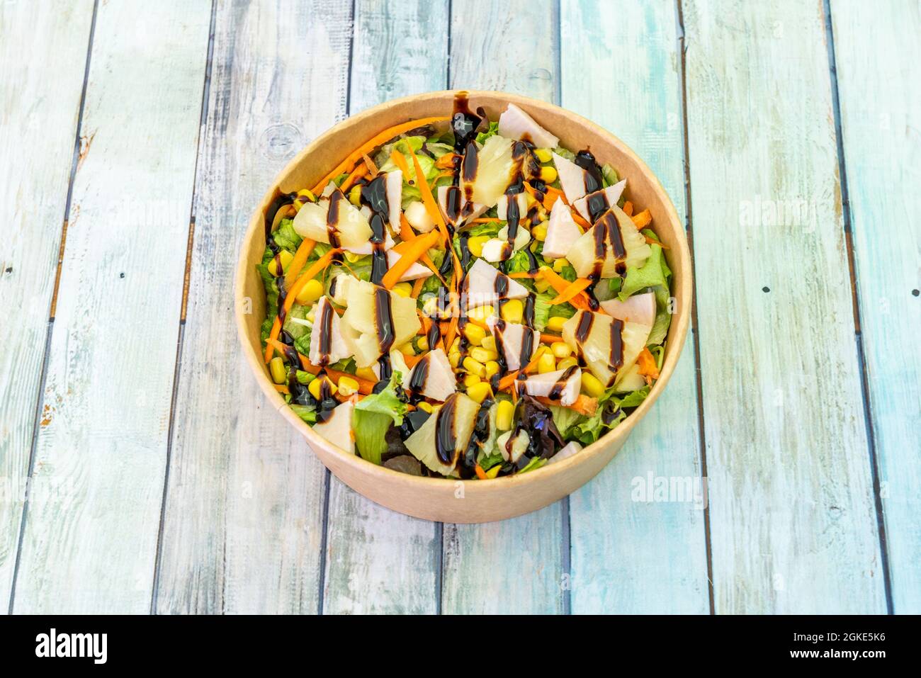 Insalata hawaiana con verdure, ananas, formaggio e prosciutto in una ciotola di cartone per la consegna a domicilio su tavoli di legno Foto Stock