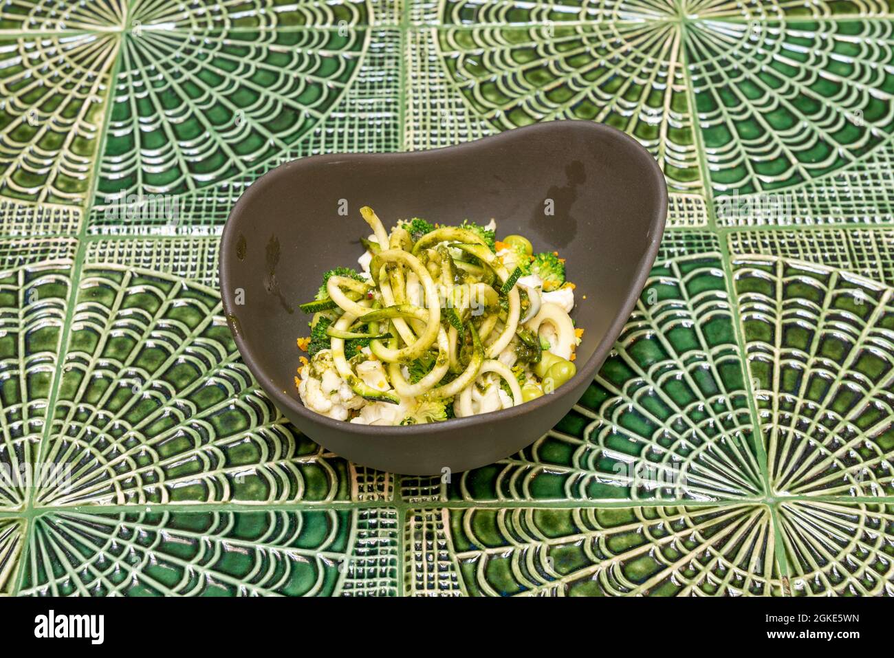 Insalata cruda di verdure croceferiche in ciotola grigia su un bel tavolo verde Foto Stock