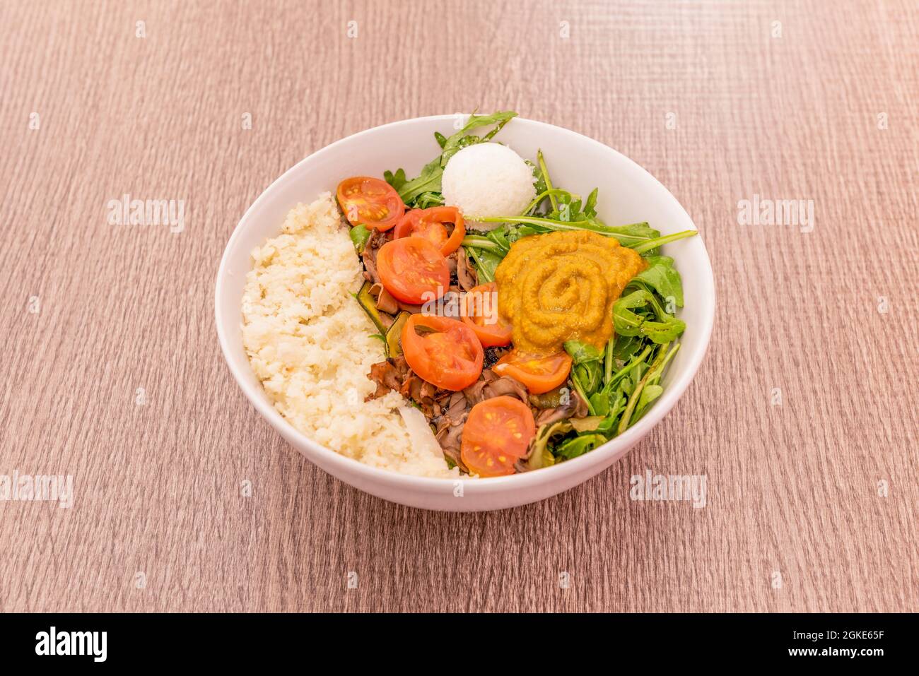 Insalata da giardino con germogli di rucola, pomodori ciliegini pelati, cocco, riso e crema di zucca su un recipiente bianco. Foto Stock