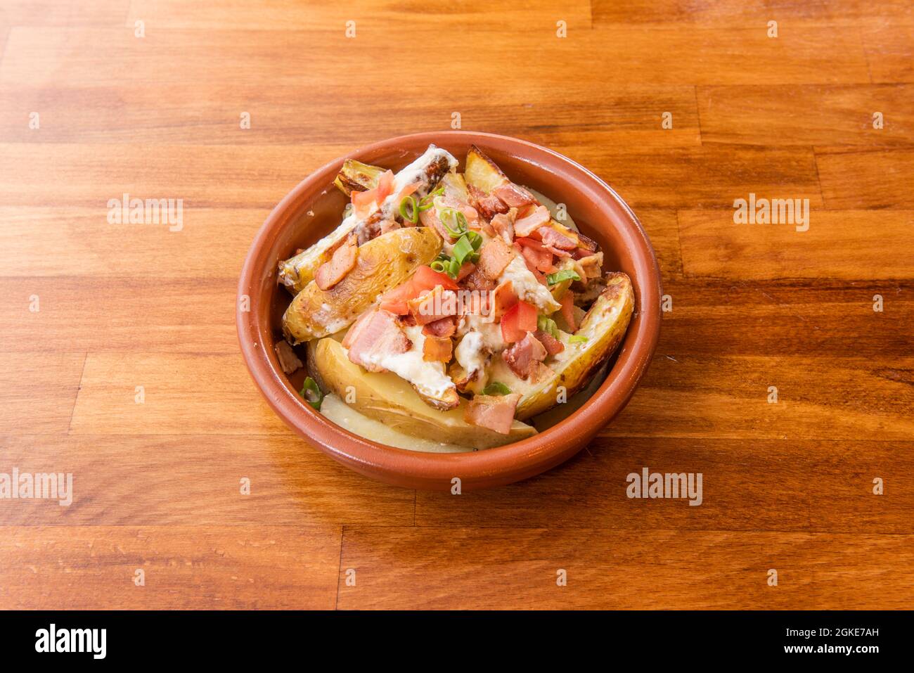 Insalata di patate arrosto con pelle, pancetta fritta a pezzi, pomodori a dadini con formaggio cremoso su vaso di argilla Foto Stock