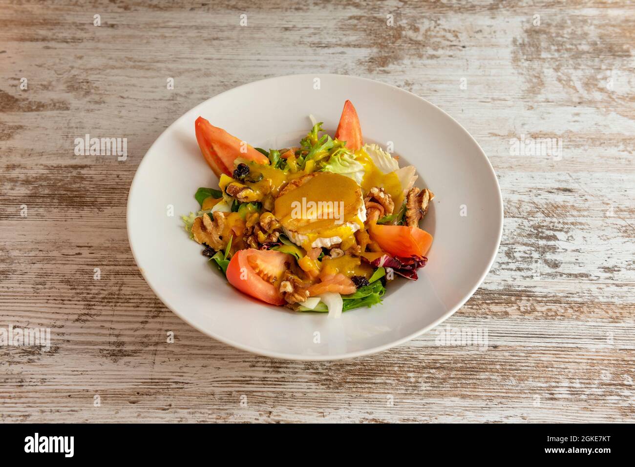 Deliziosa insalata di formaggio di capra con salsa di curry dolce, pezzi di pomodoro, lattuga e noci su un piatto bianco Foto Stock