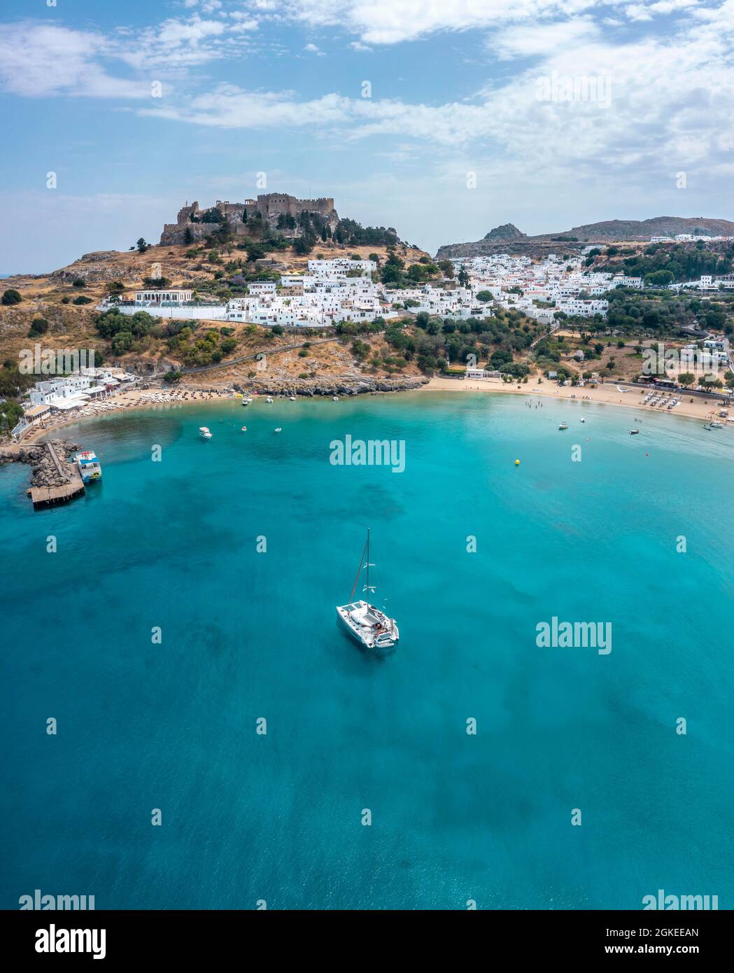 Barca a vela sul mare turchese, spiaggia sabbiosa, acropoli di Lindos, antica cittadella su una scogliera ripida, Lindos, Rodi, Dodecaneso, Grecia Foto Stock