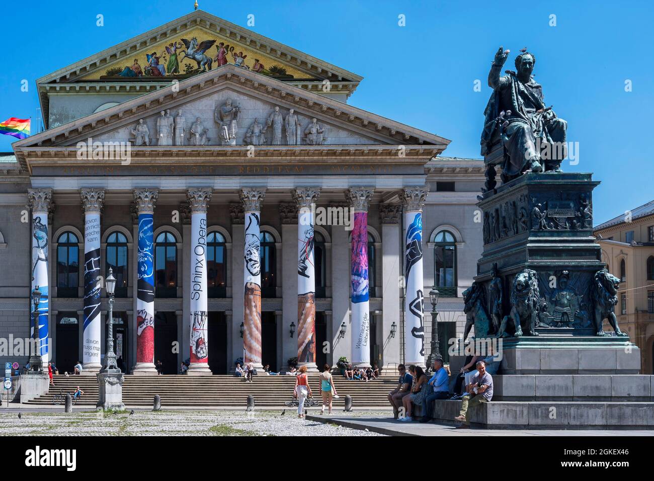 Opera, Teatro Nazionale con colonne colorate, bandiera arcobaleno e monumento di Re Massimiliano II. Joseph a Max-Joseph-Platz, Monaco, Alto Foto Stock