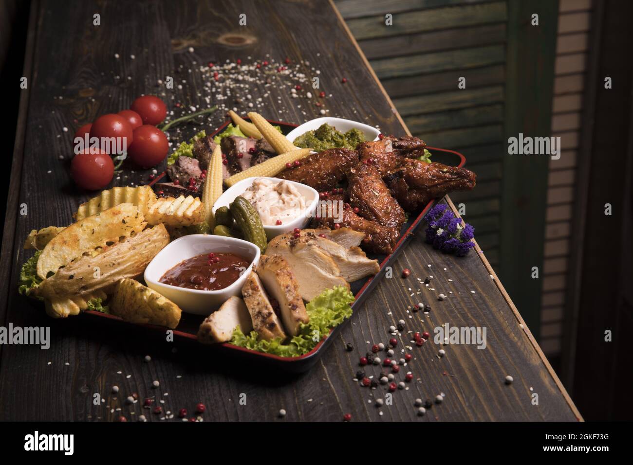 Assortimento di carne con ali di pollo fritte, manzo e maiale decorato con lattuga e pomodori ciliegini Foto Stock
