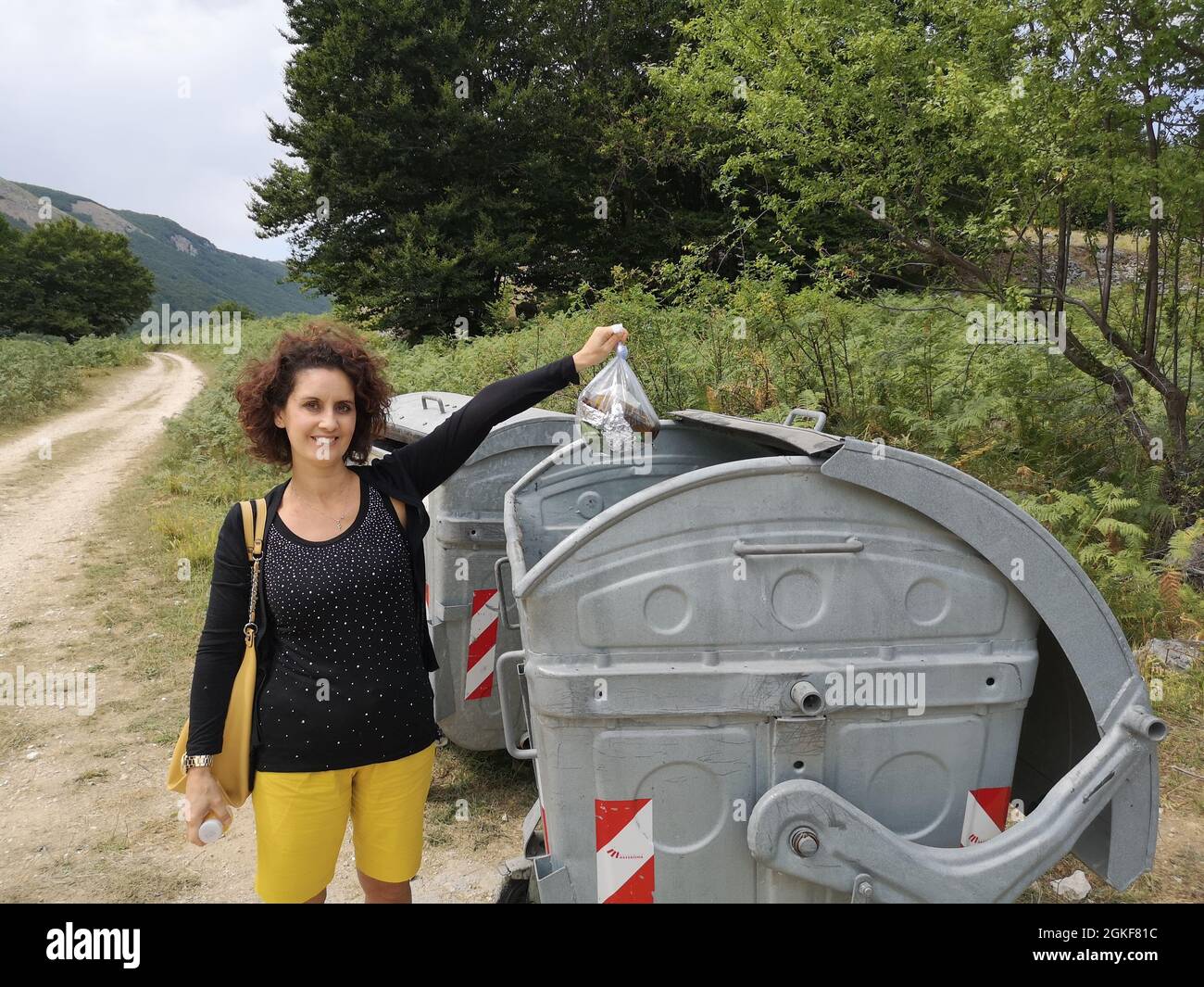 Giovane donna caucasica che getta spazzatura nel polverone in una campagna Foto Stock