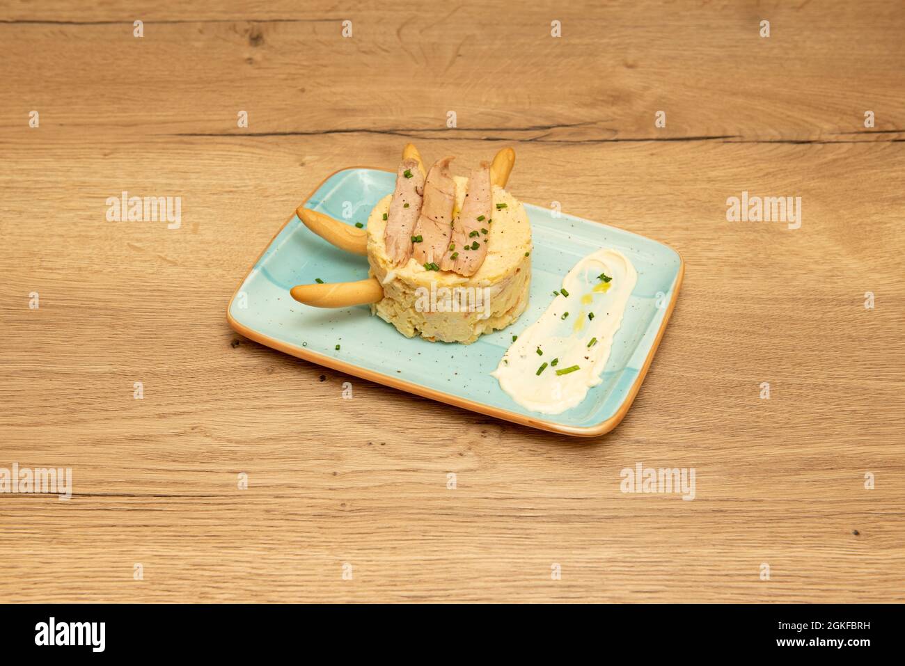 Tipica tapa spagnola di insalata russa con ventre di tonno, spikes, salsa di maionese e erba cipollina su un piatto blu Foto Stock