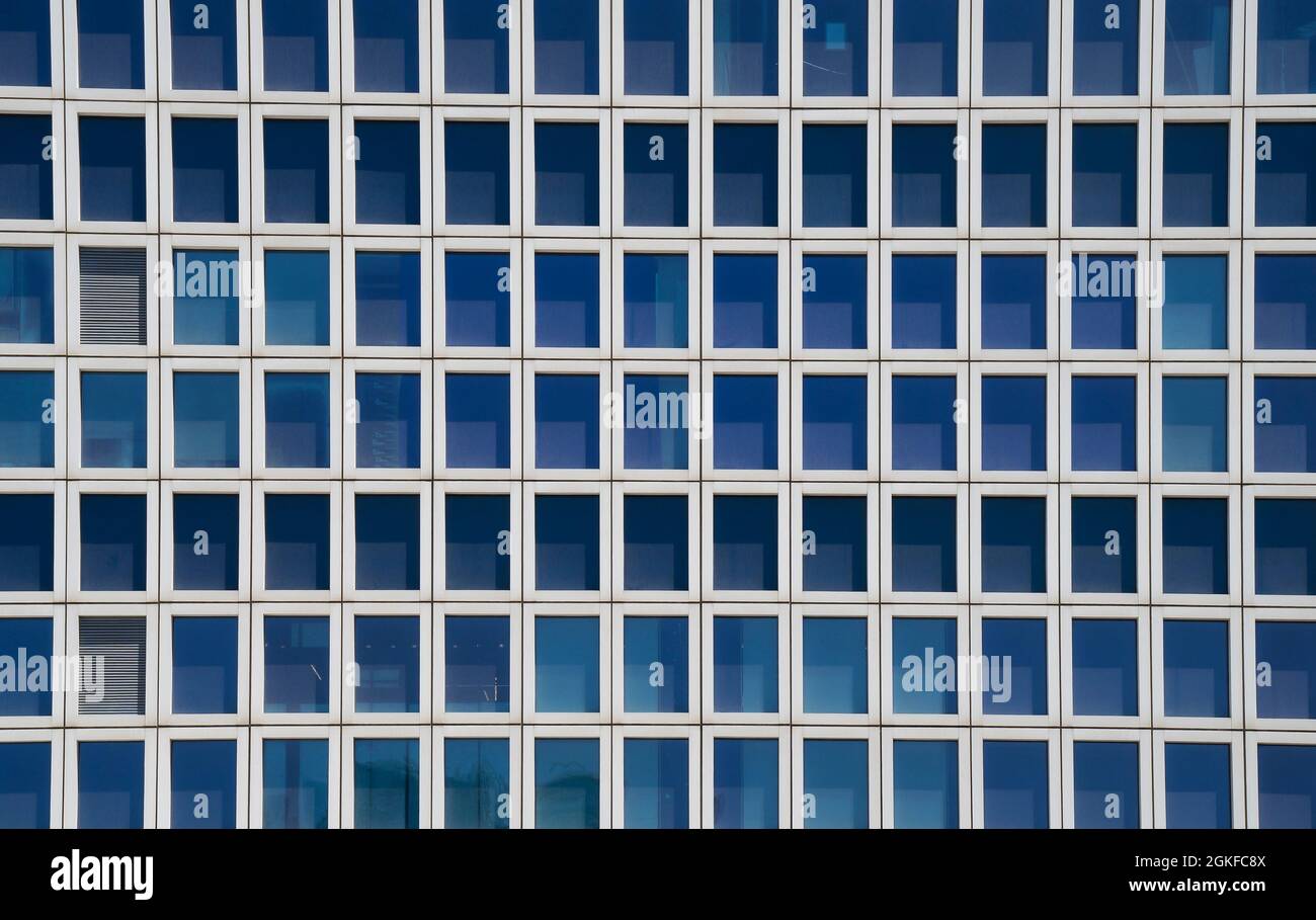 Un segmento di un tipico edificio alto, con molte finestre di vetro blu incorniciate in metallo e due persiane chiuse. Foto Stock