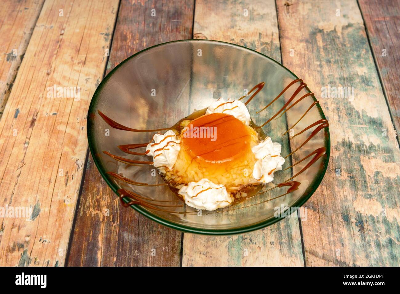 Deliziosa crema alle uova fatta in casa con crema e caramello all'interno di una ciotola di vetro su sfondo di legno Foto Stock