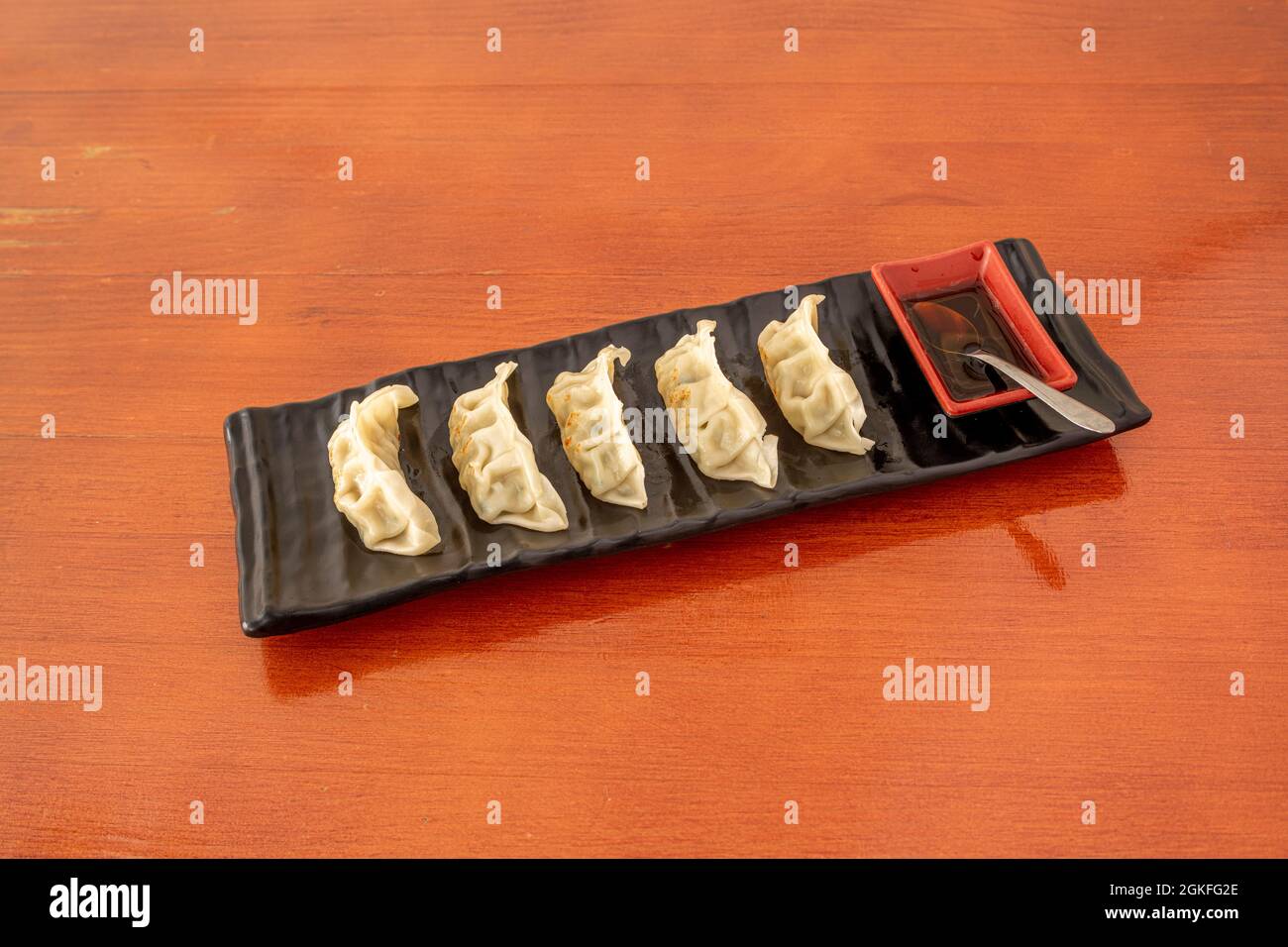 Gnocchi giapponesi cotti sul grill con salsa di soia su un piatto rettangolare nero e tavolo rosso Foto Stock