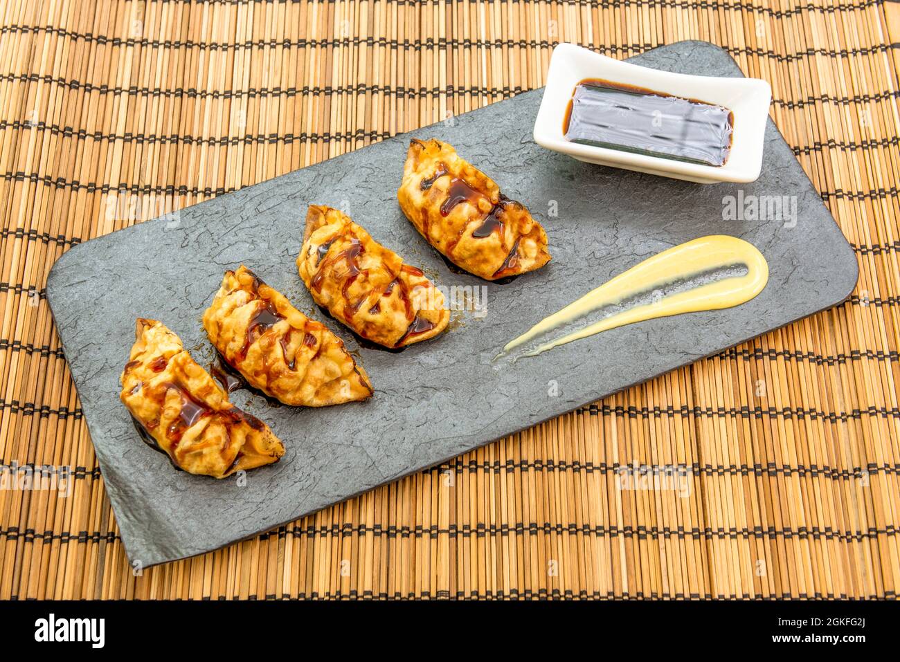 Vassoio grigio con porzione di gnocchi cinesi fritti, dim sum, salsa con soia e crema di patate su una tovaglia di bambù Foto Stock