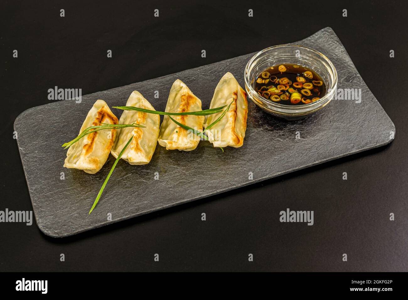 Gnocchi giapponesi, gyozas, farciti di carne al vapore accompagnati da una ciotola di soia con verdure su un piatto grigio Foto Stock