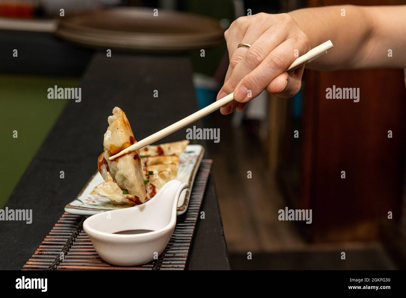 Mano della donna con i bacchetti che immergere un gyoza in salsa di soia e poi gobbling esso in su con la gioia Foto Stock