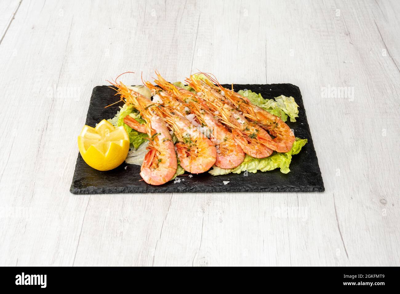 Grande porzione di gamberi fritti da Cadice sul grill e inviare su un letto di lattuga, con succo di limone, prezzemolo tritato e scaglie di sale su un ardesia nera Foto Stock