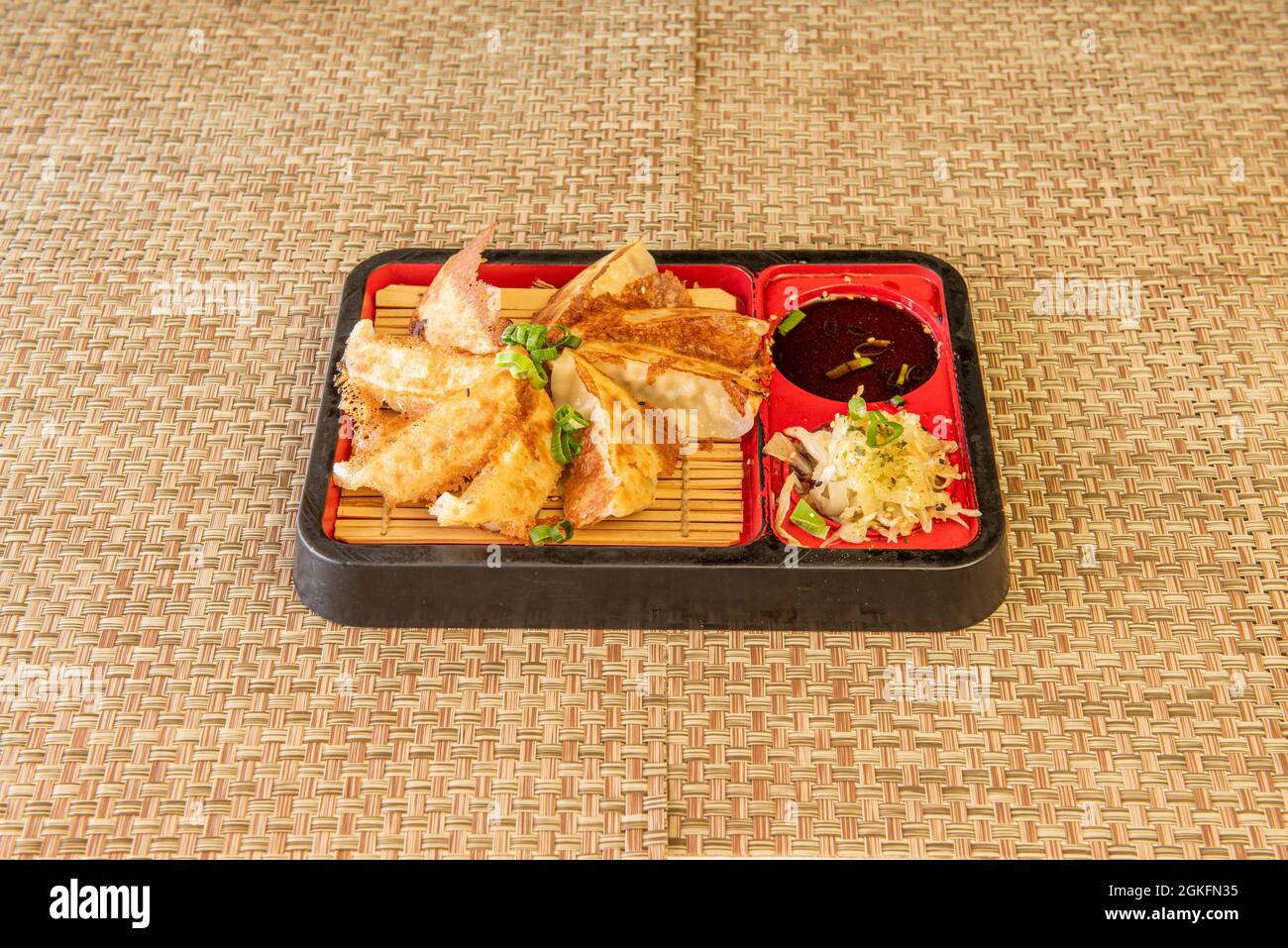 Menu giapponese di gnocchi di gyoza alla griglia, salsa di soia e verdure laterali su triumi di vimini Foto Stock