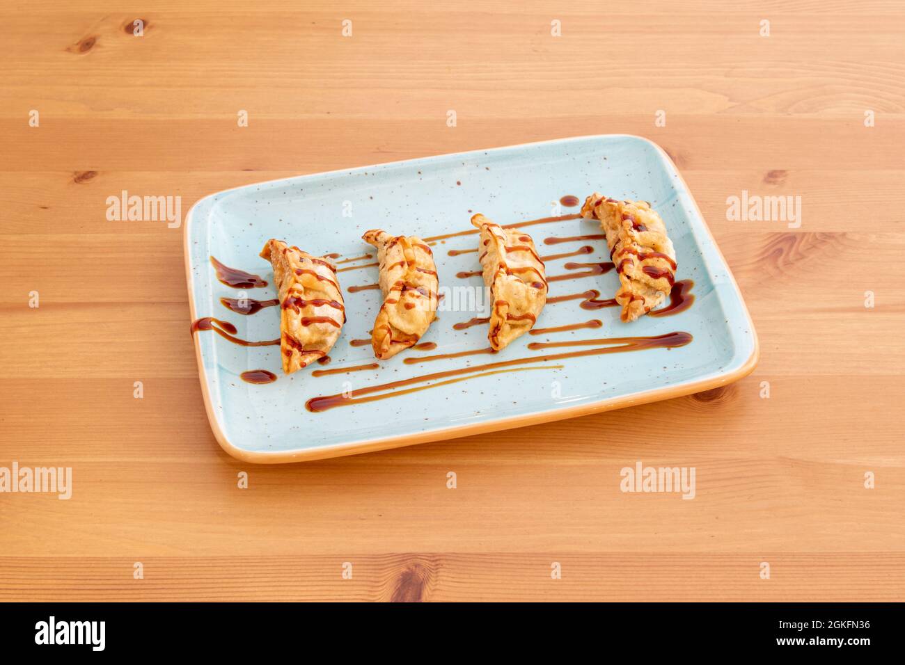 Piatto blu di gyozas gnocchi con salsa di soia in cima farcito con verdure e maiale su tavola marrone Foto Stock