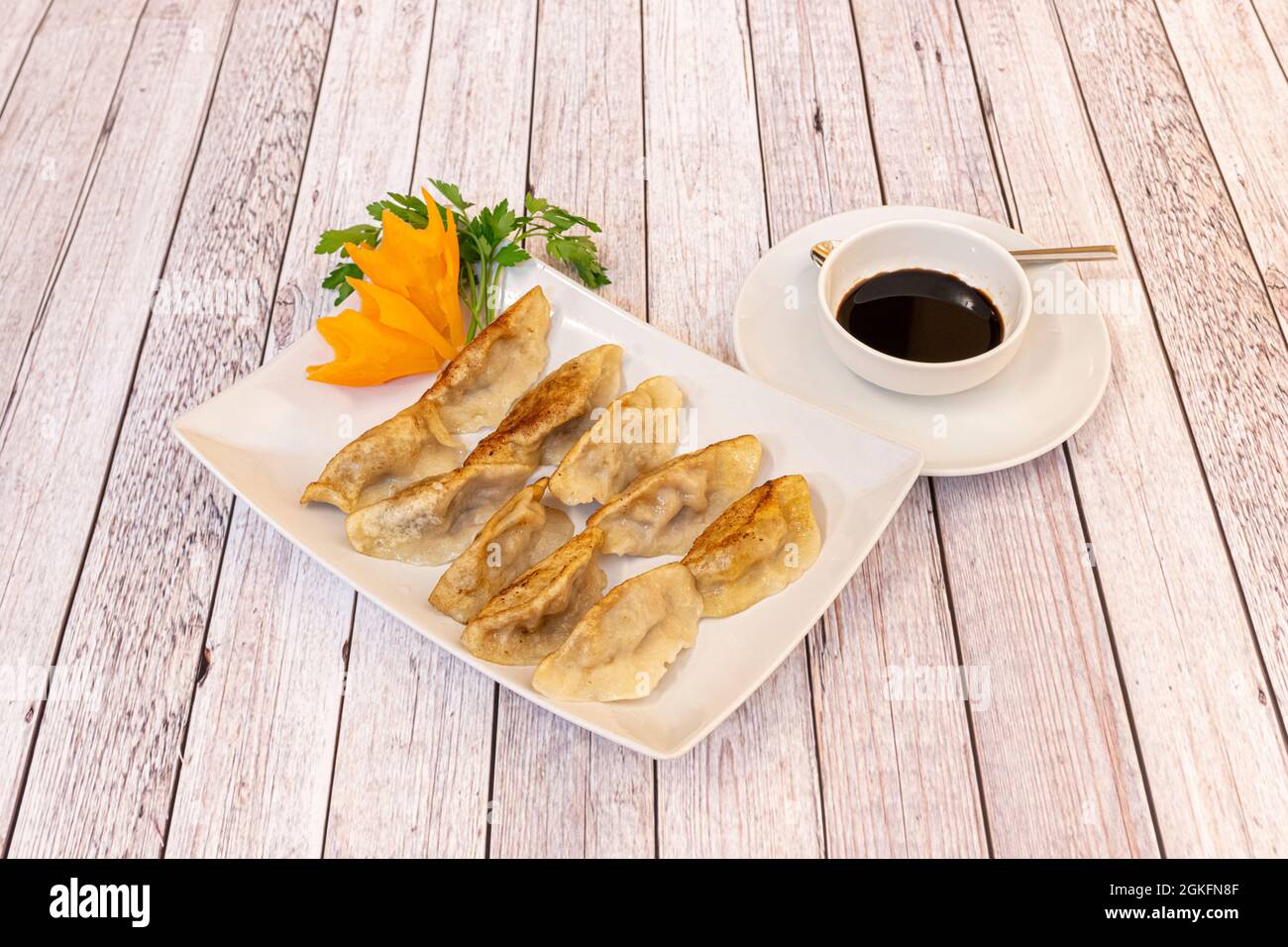 Tipiche polpette giapponesi cotte sulla griglia gyozas con un fiore di carota e salsa di soia in un recipiente bianco su un tavolo chiaro Foto Stock