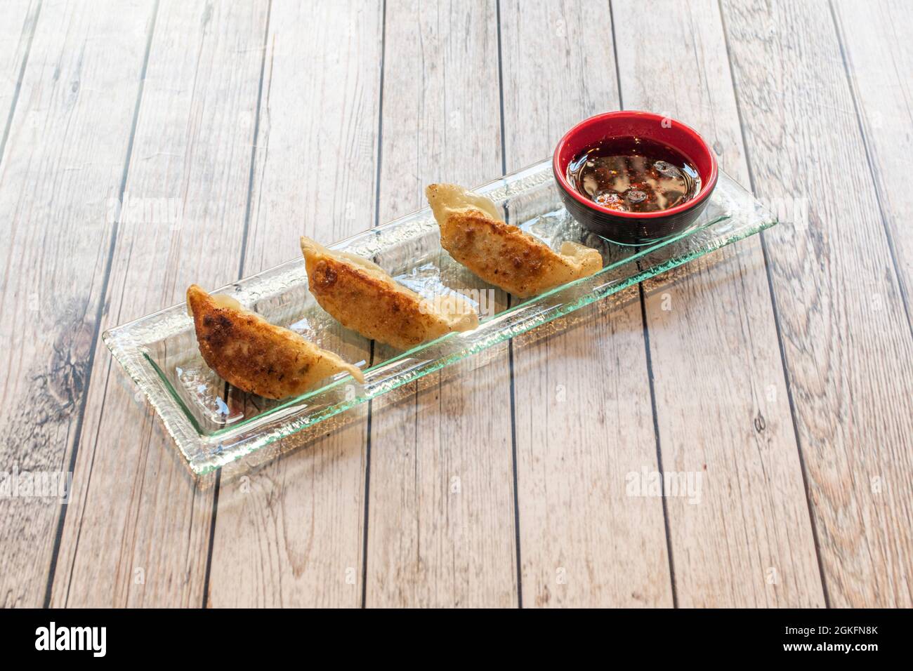 Antipasto di gyozas fritto alla griglia con salsa di soia su un bel vassoio di vetro su un tavolo di legno chiaro Foto Stock