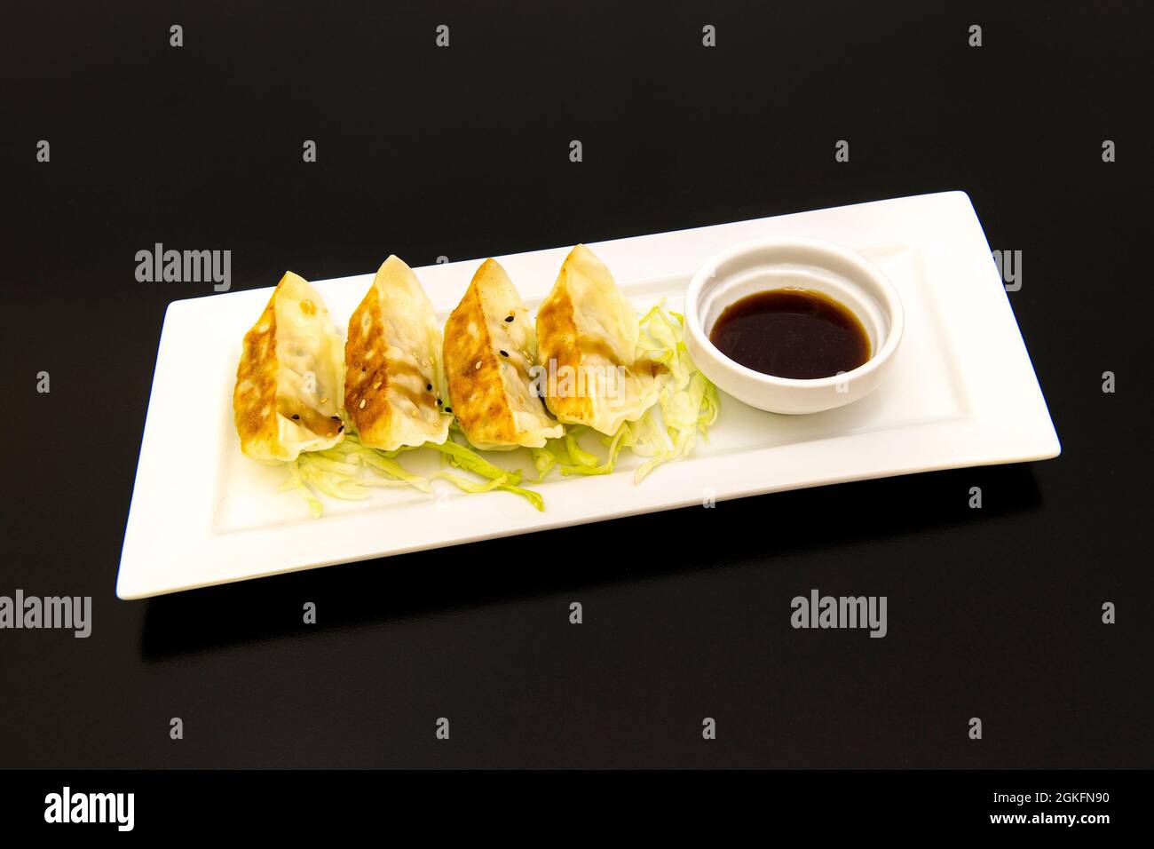 Gyozas cinese alla griglia con una ciotola di salsa di soia per immergere su un piatto bianco Foto Stock