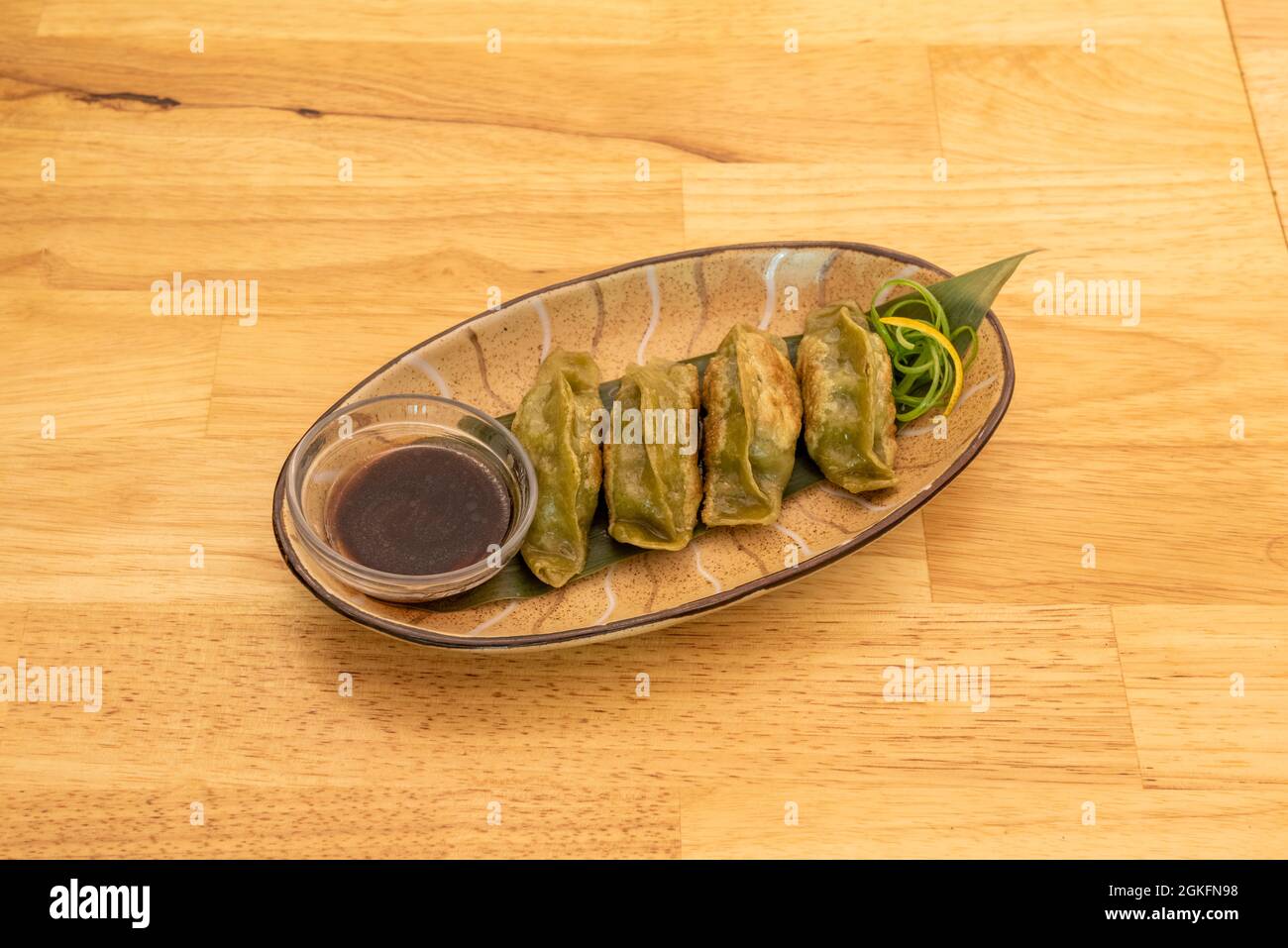 vassoio di gyozas di verdure fritte sulla griglia con salsa di soia su una foglia di banana e tavolo di legno Foto Stock